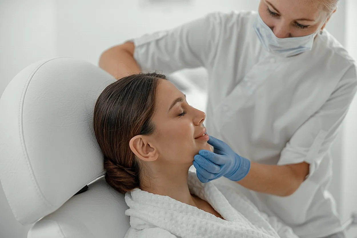 mujer en silla recibe tratamiento facial por parte de profesional con mascarilla y gauntes